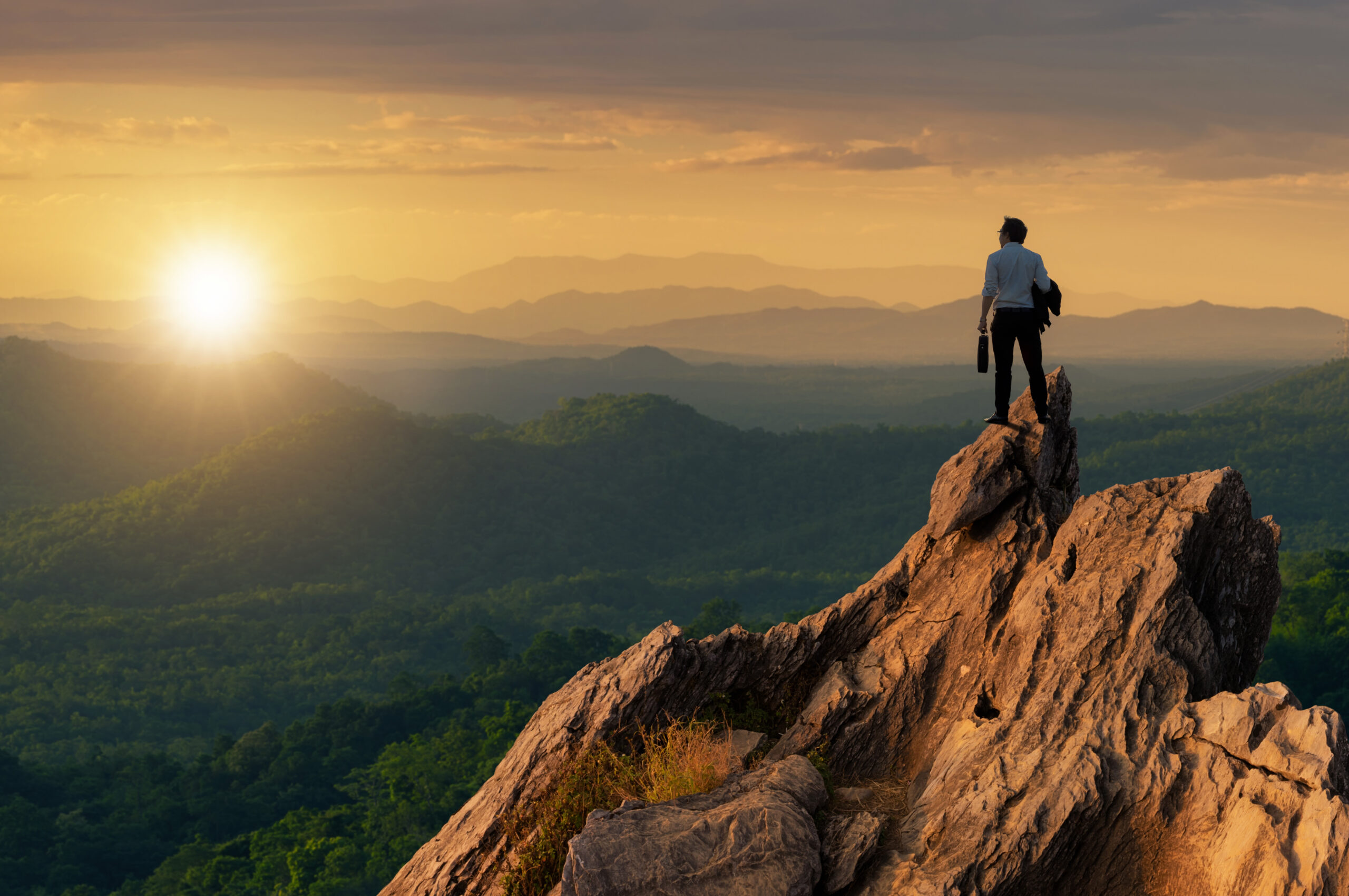 Business person on mountain top overlooking the sun rising on the horizon